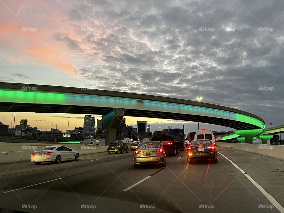 Commuting home by car at the end of a workday. The evening sky and cars turning on their lights on the highway.