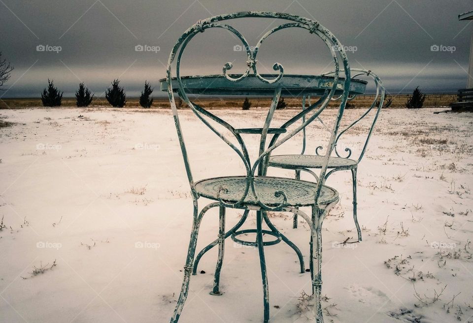 Waiting on Spring...a sad ice cream table with two heart shaped chairs in an empty yard full of snow on a dark gray day.