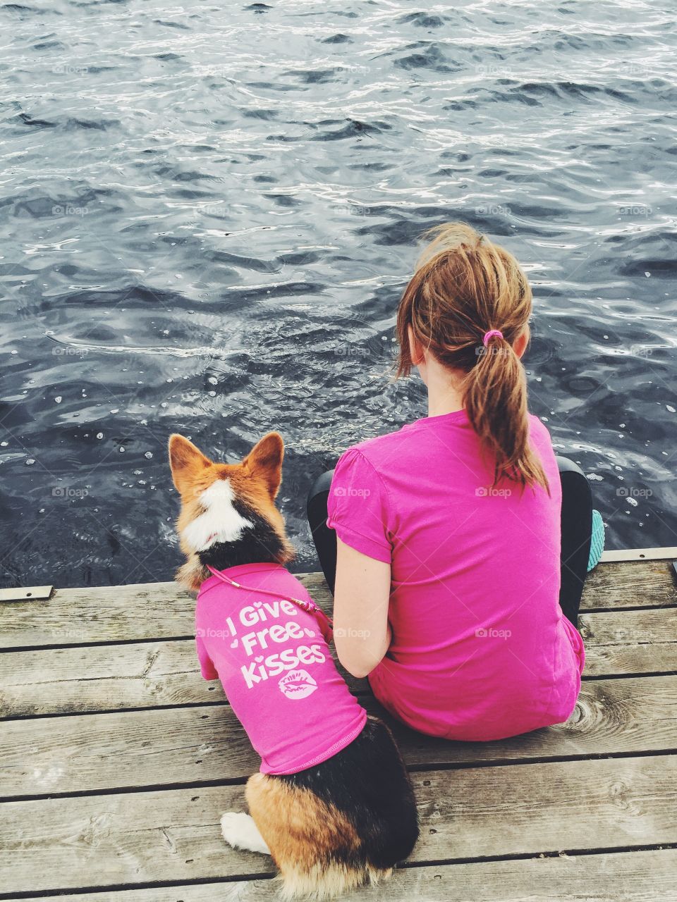 Girl and her dog dressed in pink sitting on a bridge an playing with the water