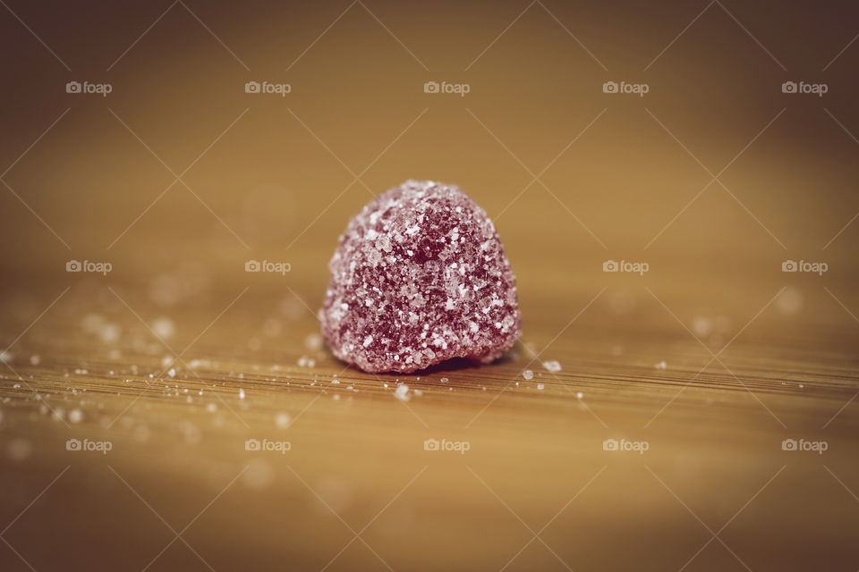 A macro portrait of a red piece of candy sprinkled and surrounded by sugar on a wooden table.