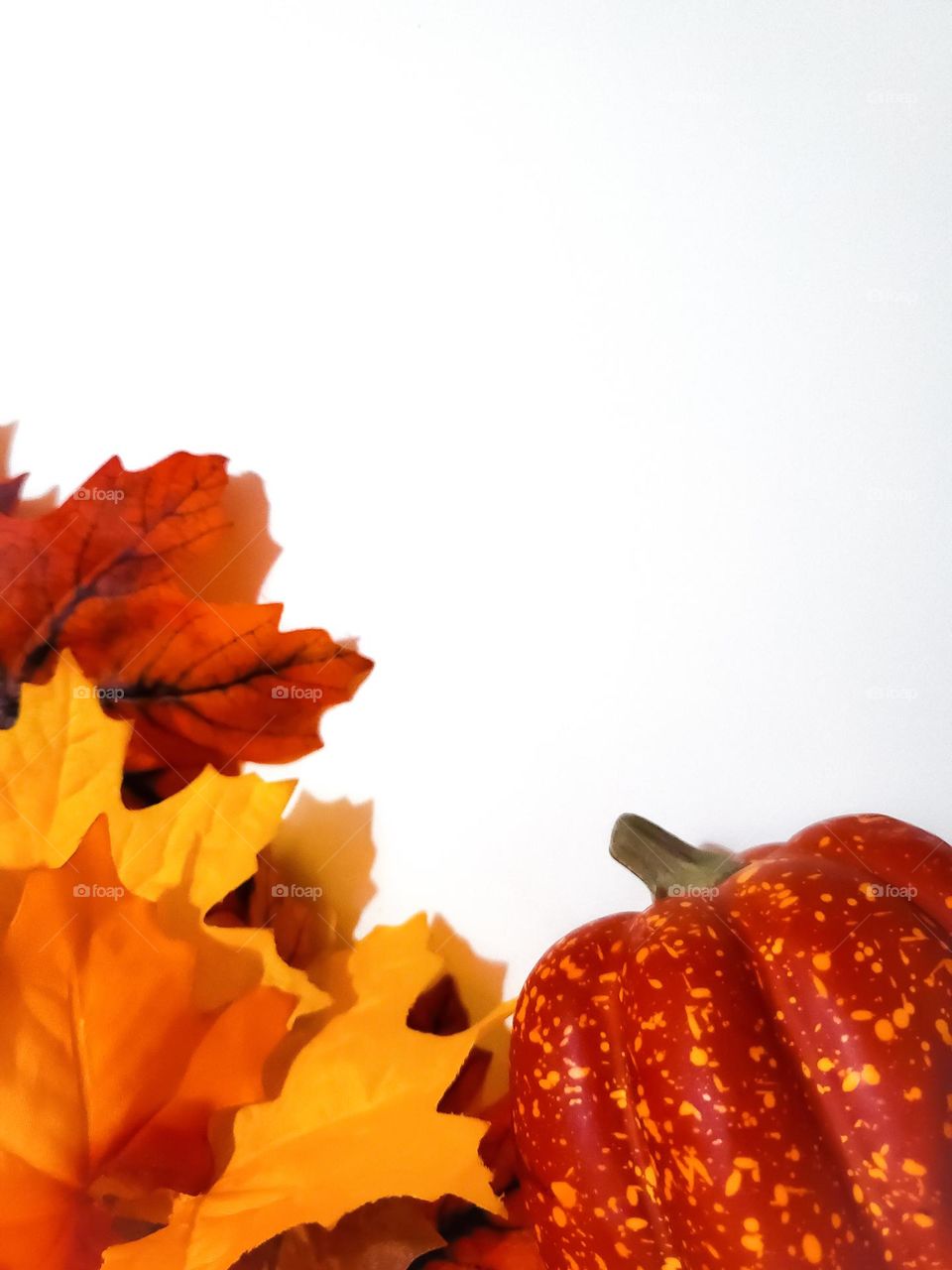Faux pumpkin and faux fall leaves on a white background.