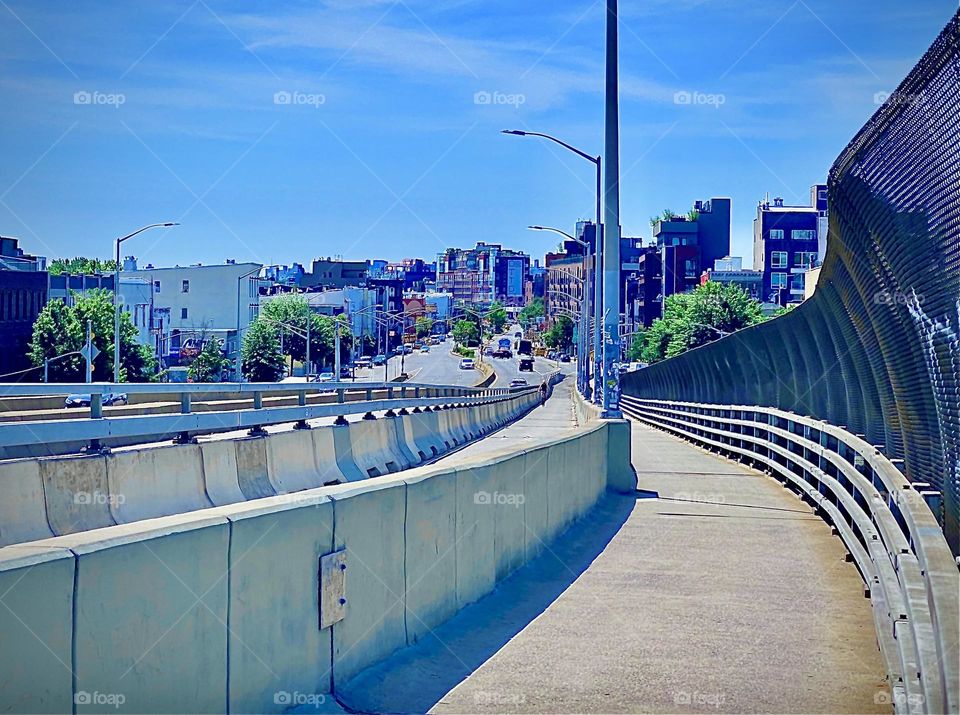 A view of the pedestrian lane of the “Pulaski Bridge” facing in the opposite direction towards “Greenpoint, Bklyn”. The bridge takes a downhill turn on either side. The edges are securely fenced off and protected. 2022. Hypnotic Productions
