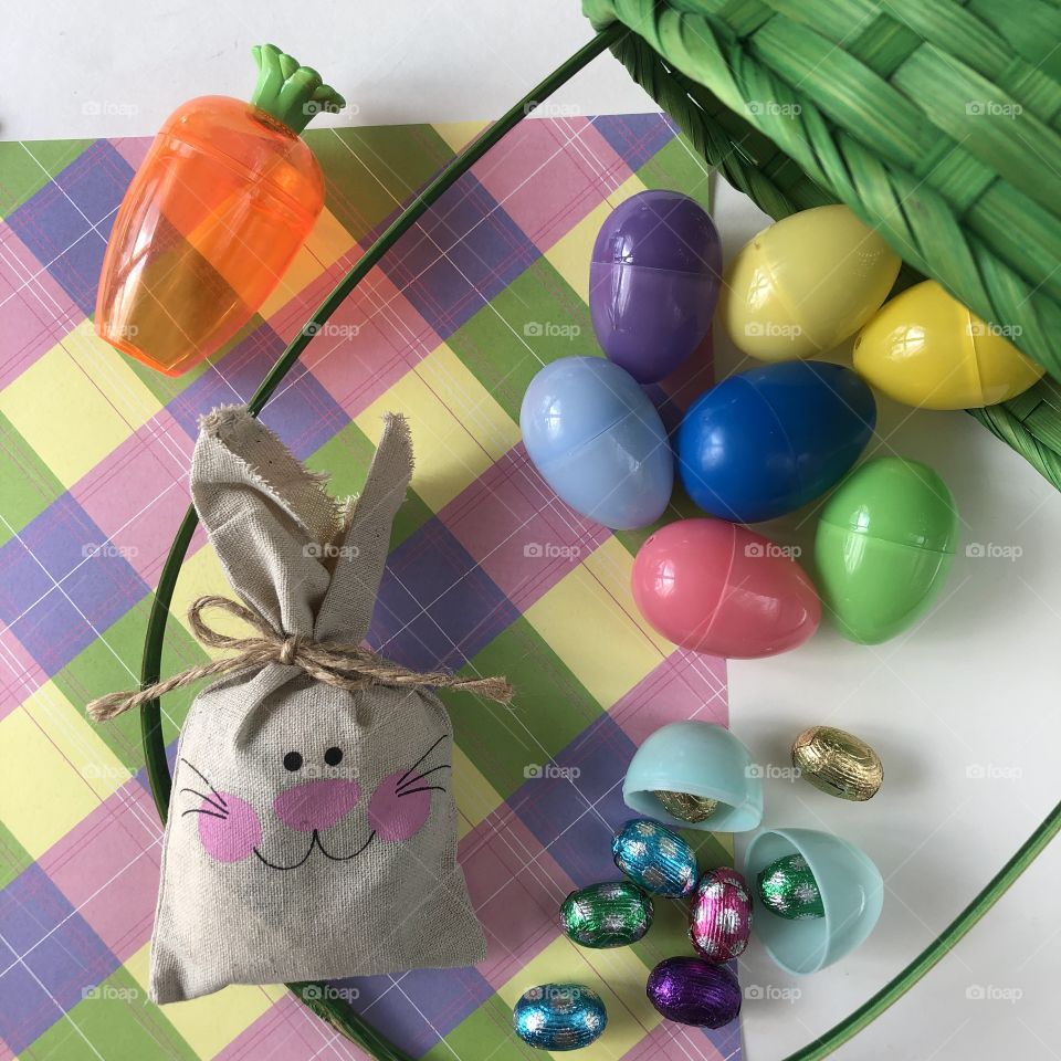 Easter flat lay with plastic eggs ready for a hunt, falling out of a basket with chocolate and a rustic Easter bunny in pastels