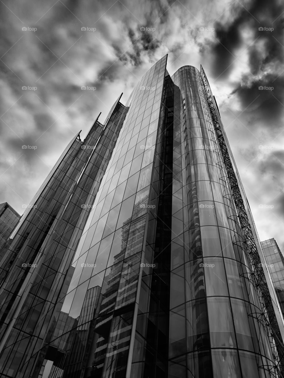 edificio cubierto de vidrio, moderno, visto desde abajo, reflejando las nubes  en blanco y negro
