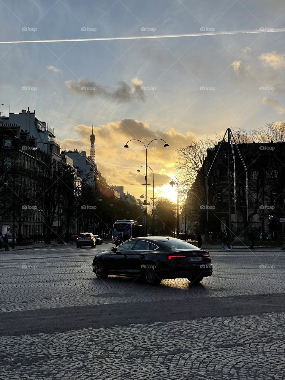 A car is on world’s beautiful avenue “ Champs Élysées in Paris “ where sun is disappearing inside clouds 