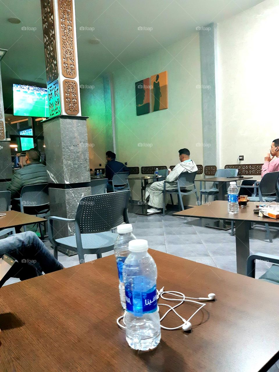 : An image inside a café in Bayt Melloul showing a group of people enjoying their drinks and engaging in conversation in a calm atmosphere. The ambiance is warm with soft lighting, and distinctive details like modern furniture