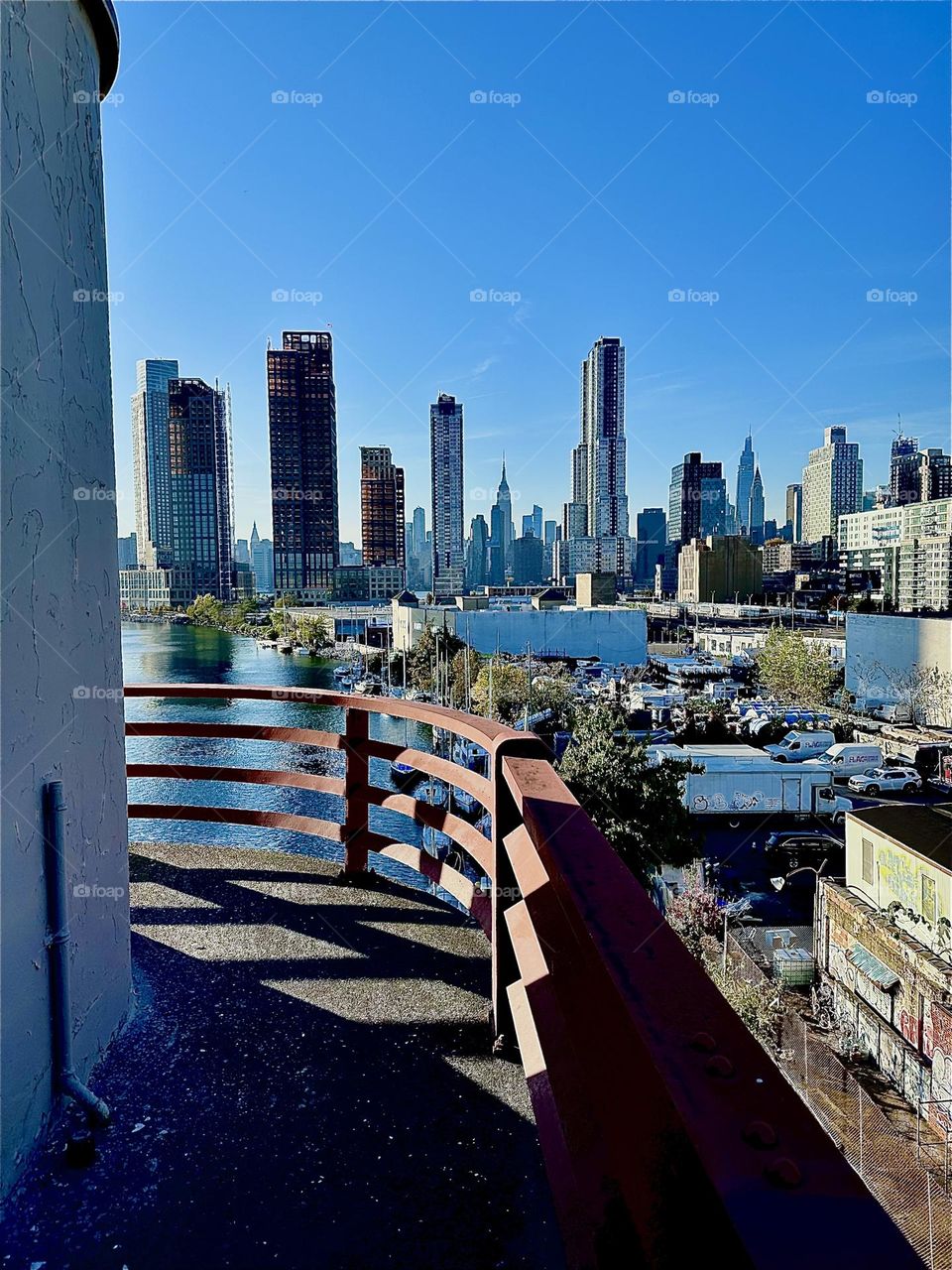 This is “Newtown Creek” seen from the center outpost of the “Pulaski Bridge” in LIC, Queens that it connects to “Greenpoint”, Brooklyn. In the distance “Manhattan” incl. the “Empire State Building” is visible. 2023. Hypnotic Productions