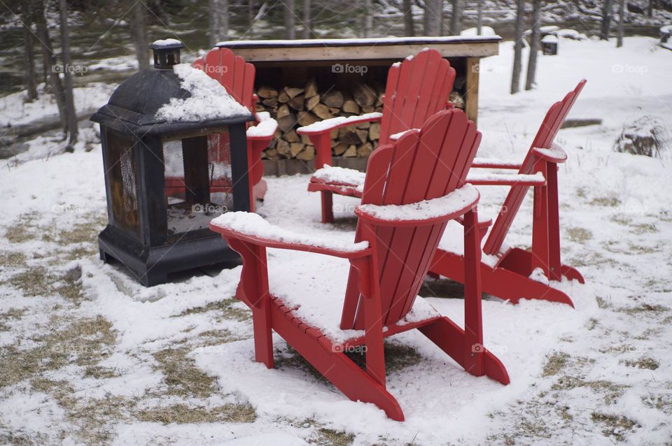 Red Muskoka chairs surround an outdoor fire waiting to be warmed.