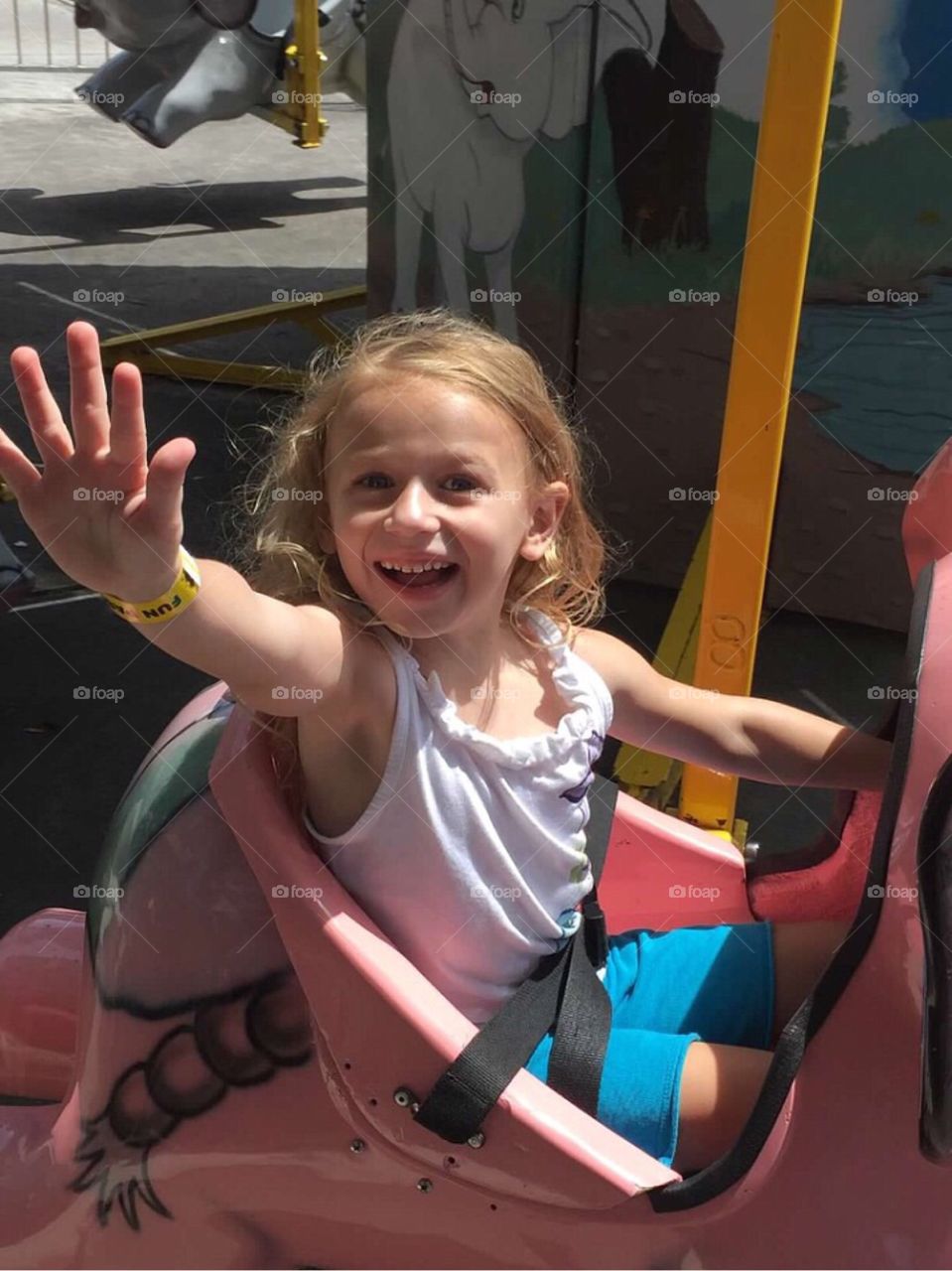 A little girl waving hello as she rides a ride at the amusement park. 