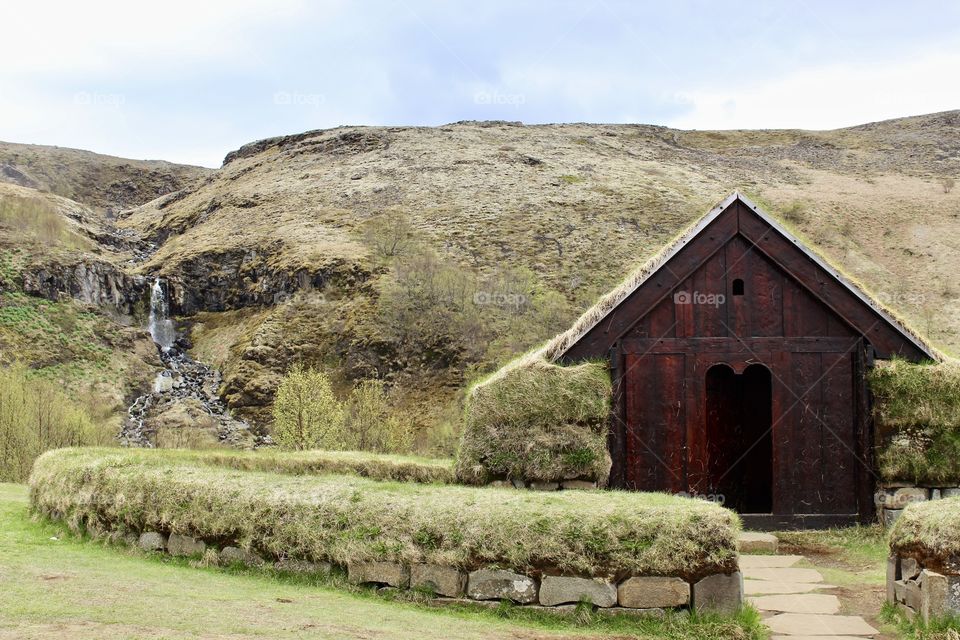 Small Viking village church in the countryside of Iceland. Small waterfall in the background