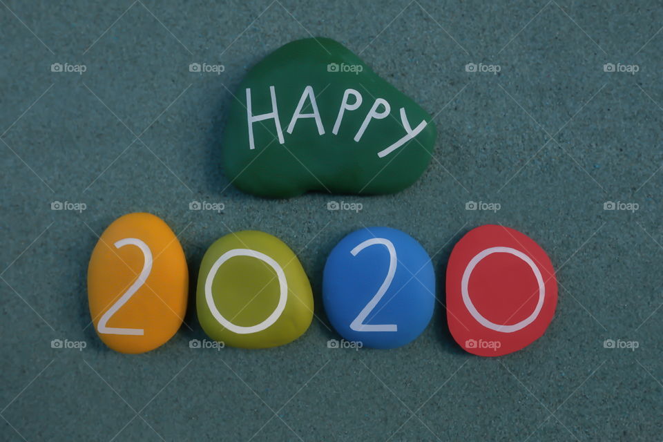 Happy 2020 celebrated with a composition of colored and carved stones over green sand