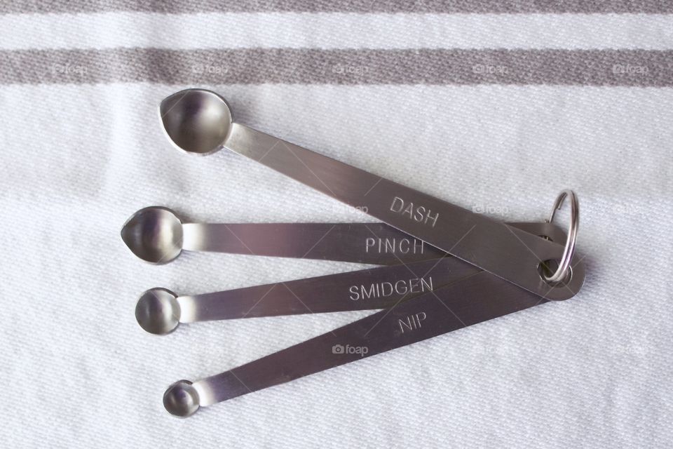 Overhead view of miniature stainless steel measuring spoons on a white-and-grey-striped dish towel