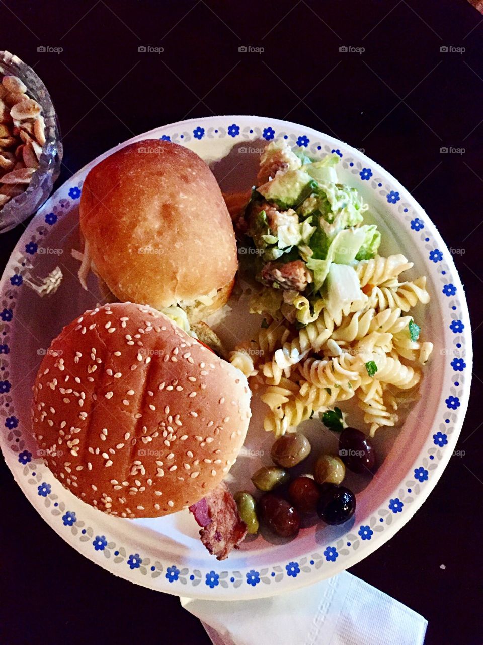 Summer lunch,  hamburger, pulled pork on a bun, pasta salad, ceasar salad, green and black olives. 