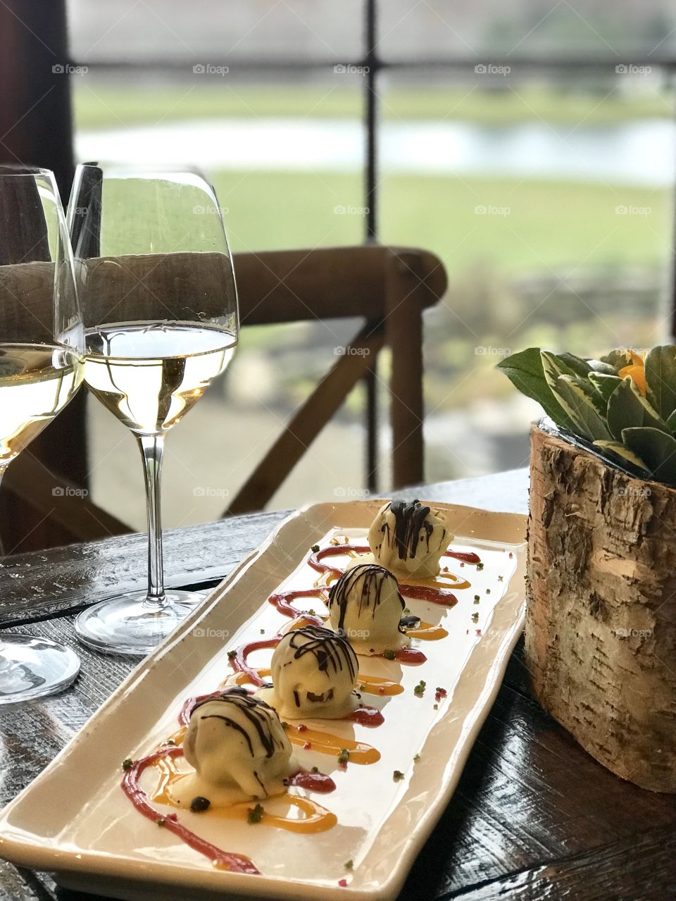 Dessert truffles on white plate with two glasses of wine with view of the outdoors in background 