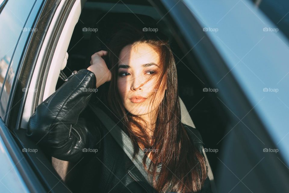 Sad beautiful charming brunette long hair young asian woman in black leather jacket in car window