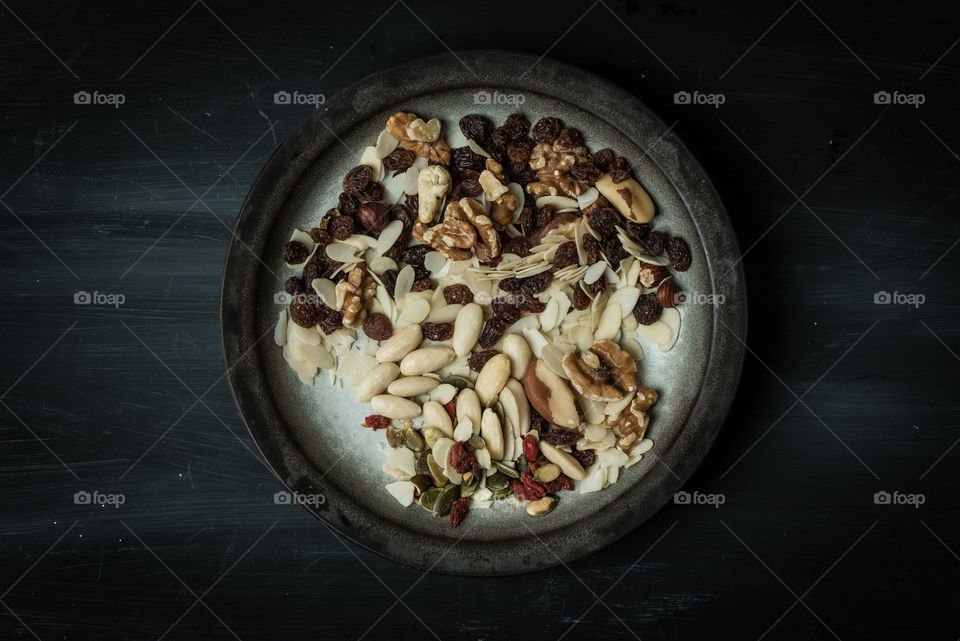 dark food photography. rustic, black, wooden table with vintage plate full of nuts. top view