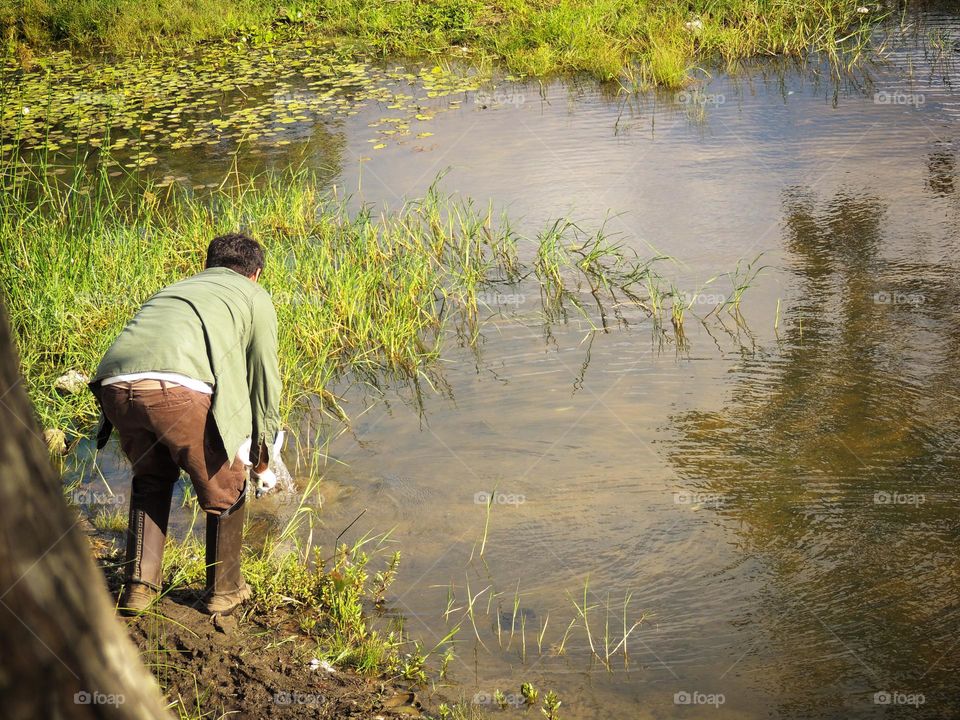 A men all dressed up in clothes to protect from the sun, collecting something from the river wishing for better days 