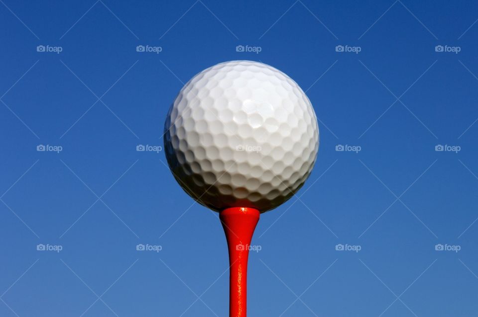 Golf ball on red tee with sky as a background