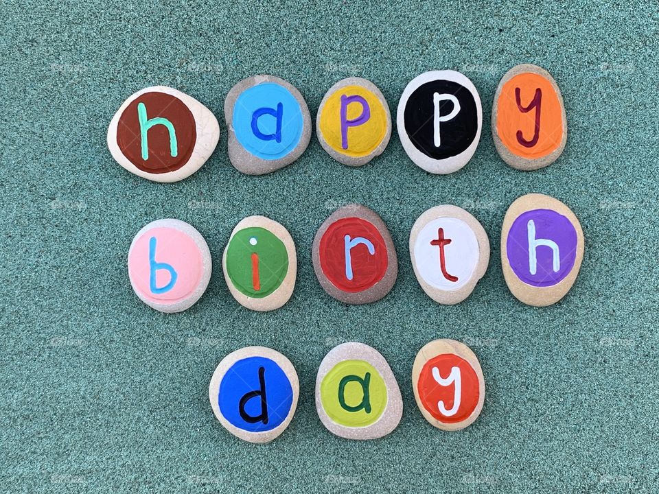 Happy Birthday text composed with creative colored stone letters over green sand 