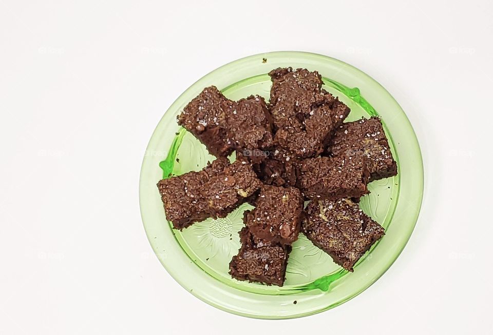 Chocolate brownies on a green glass plate with a white background 