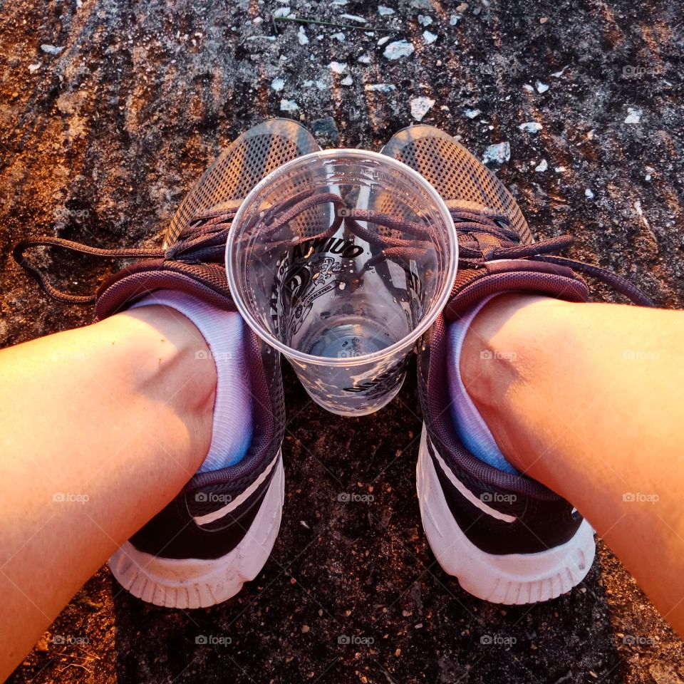An empty plastic cup between black sports shoes