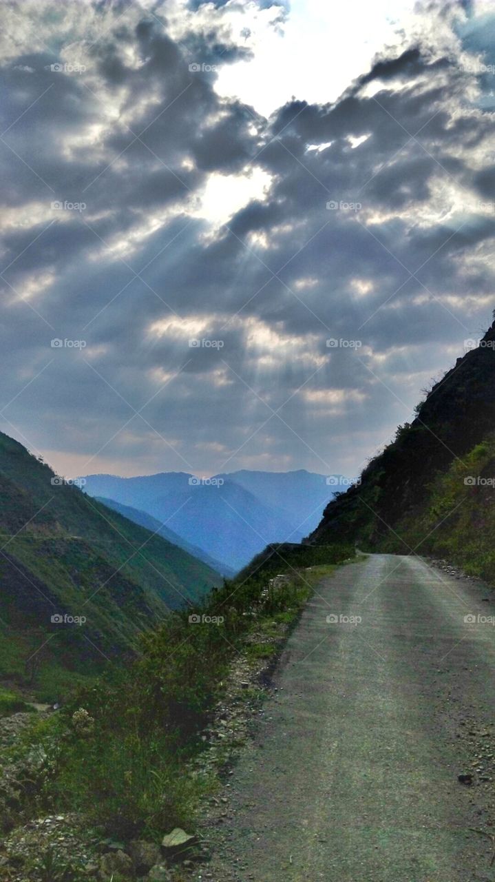 mesmerising view of the road throught the hills with sun battling agains clouds overhead
