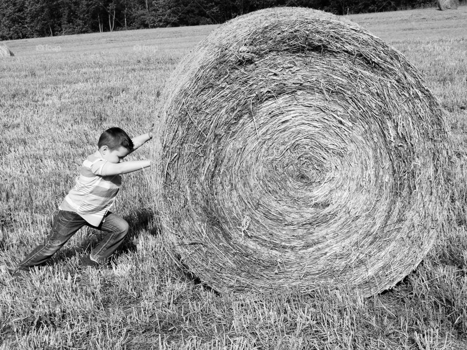 little boy trying to push large hay bale