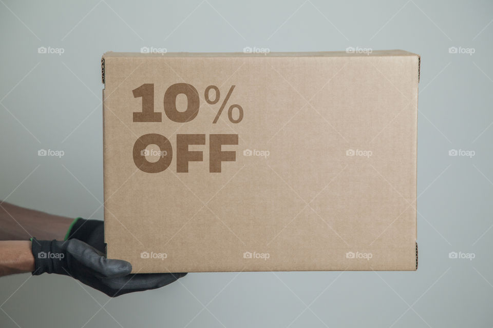 Cardboard box with 10% off order written on the box placed on the floor in an empty room with a neutral background. delivery concept. economy concept. business concept. shopping concept. copy space.