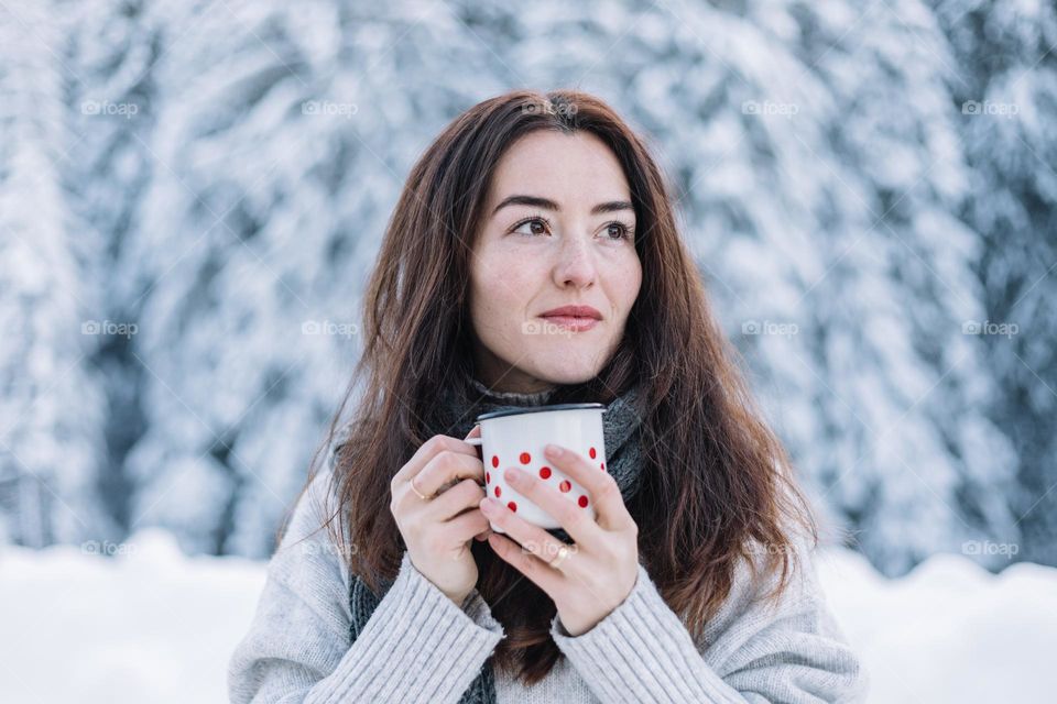 Beautiful young woman surrounded by a white landscape, while being on a road trip in the mountains, in winter time.