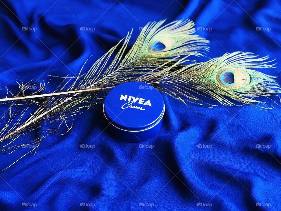 Nivea cream with peacock feathers and blue background.