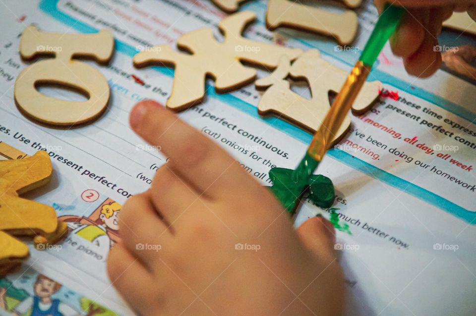 The boy paints wooden letters in different colors.