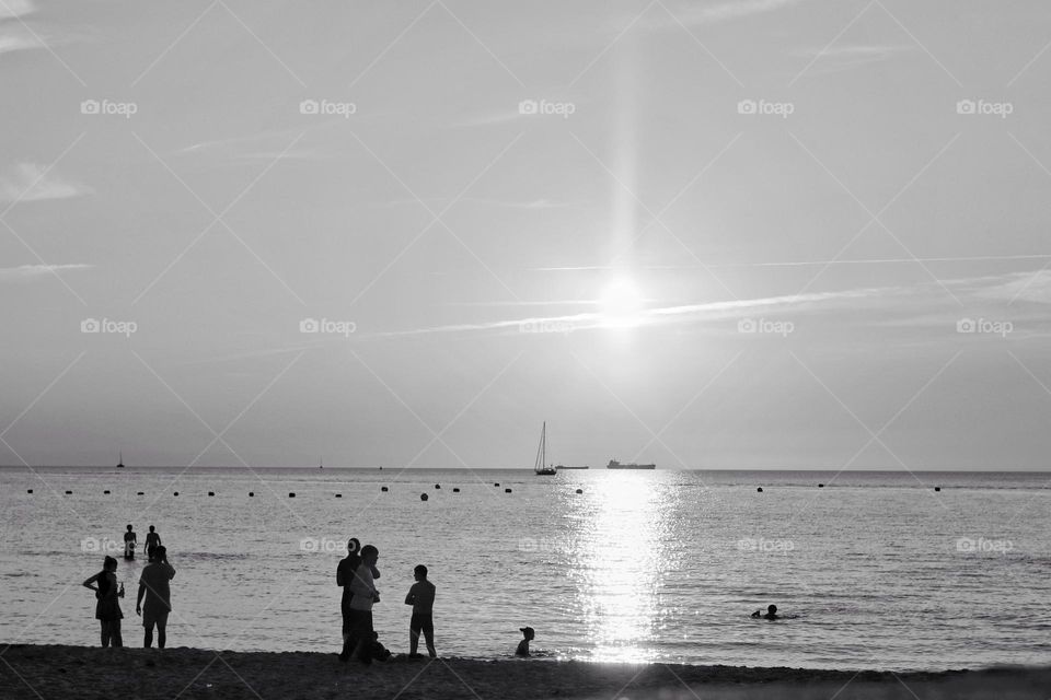 Black and white photo of people silhouettes on the beach and in the water in the sunset in the backlight