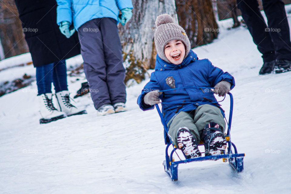 The boy is sledding and is very happy without hiding his emotions