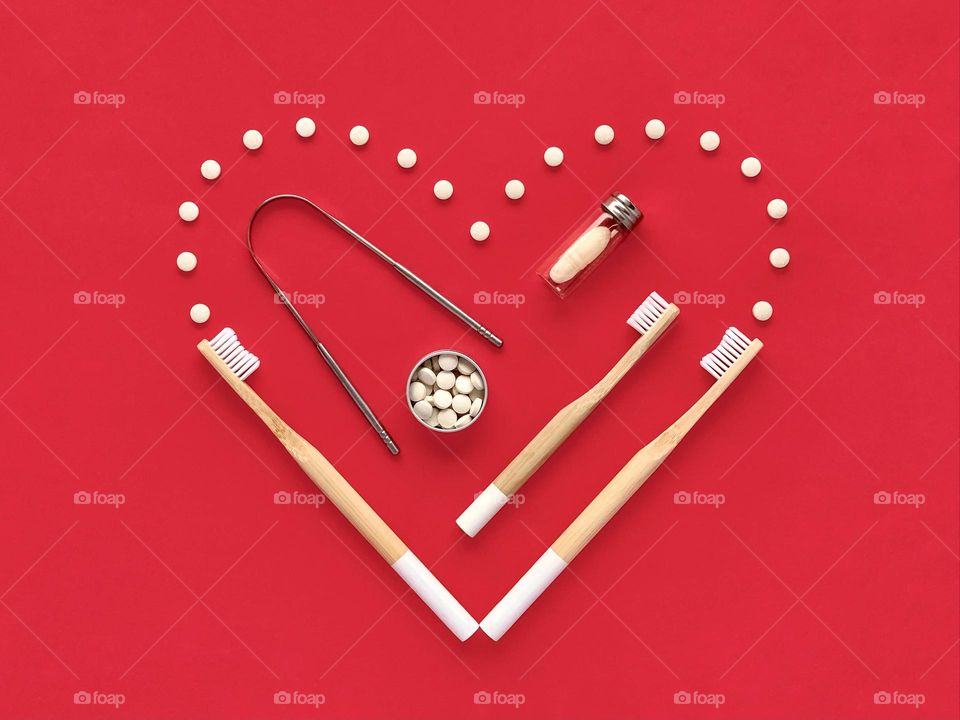 Bamboo toothbrushes, toothpaste, dental floss, tongue cleaner. Creative heart on the red background.