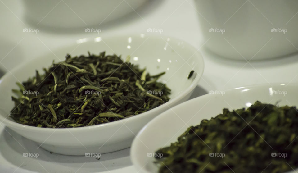 Green tea leaves in white porcelain bowls closeup detail 