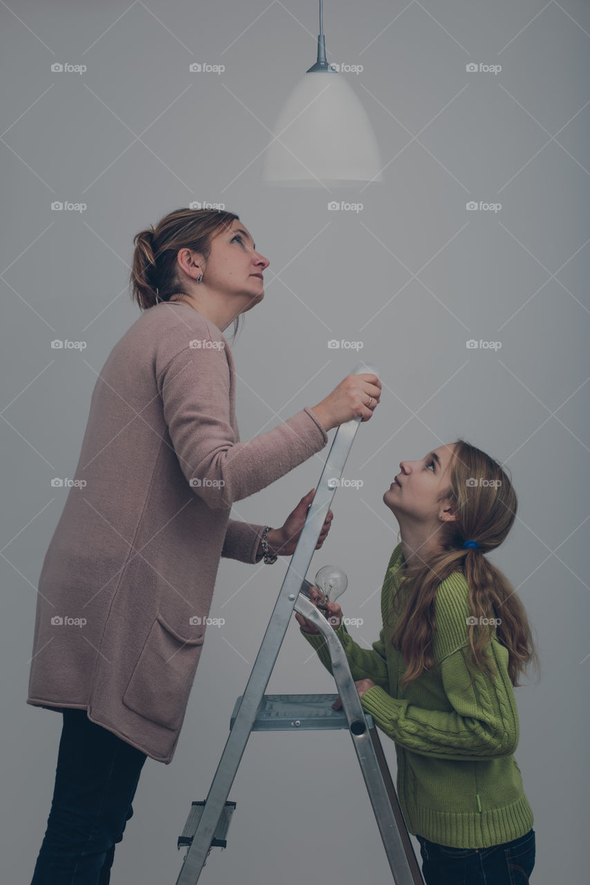 Mother and daughter standing on ladder changing light bulb