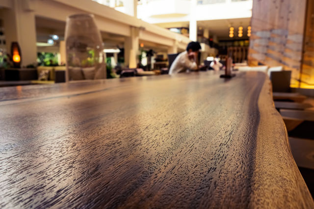 Waikiki, Honolulu, Hawaii, USA - December 15, 2015: Lounge area of the Waikiki Beach Marriott Resort and Spa Hotel. Public accesses this area frequently. Image features warm color and a person seated at a long wooden table reading. Image emphasizes on the textured table top.
