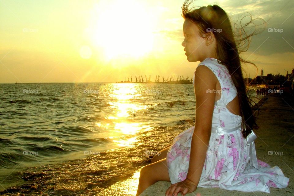 little girl seats on the shore and looks into a distance