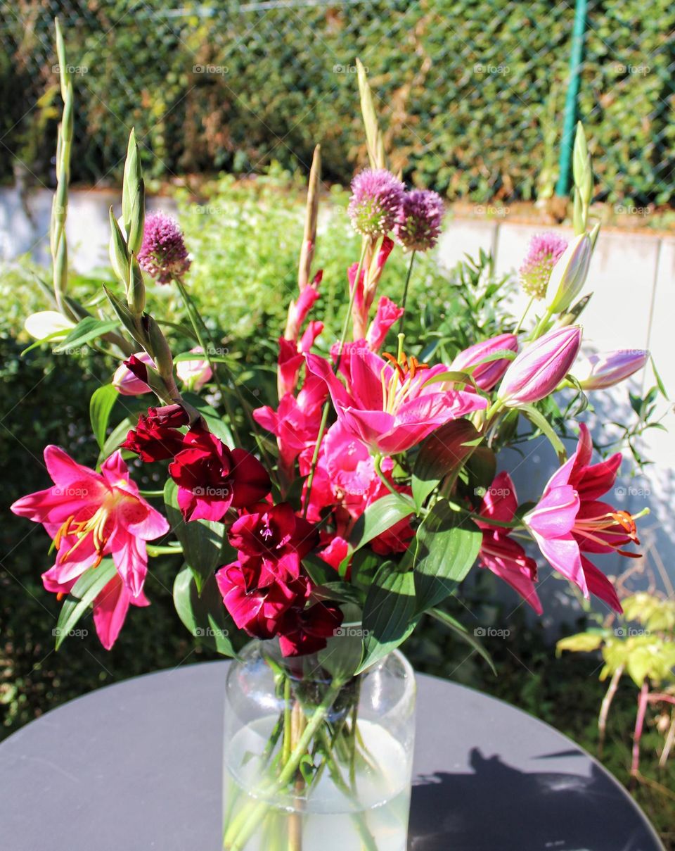 Pink oriental lilies and other pink flowers in a vase standing on a garden table.