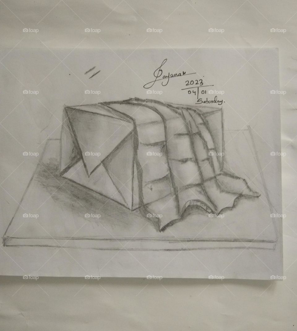 This is a capture of a pencil art of a object drawing.There is a box covered with a piece of cloth.All of these objects are on a flat surface.there is the date of the finishing this scratch ,the signature of the artist.it's sanjana and that's me.ππ
