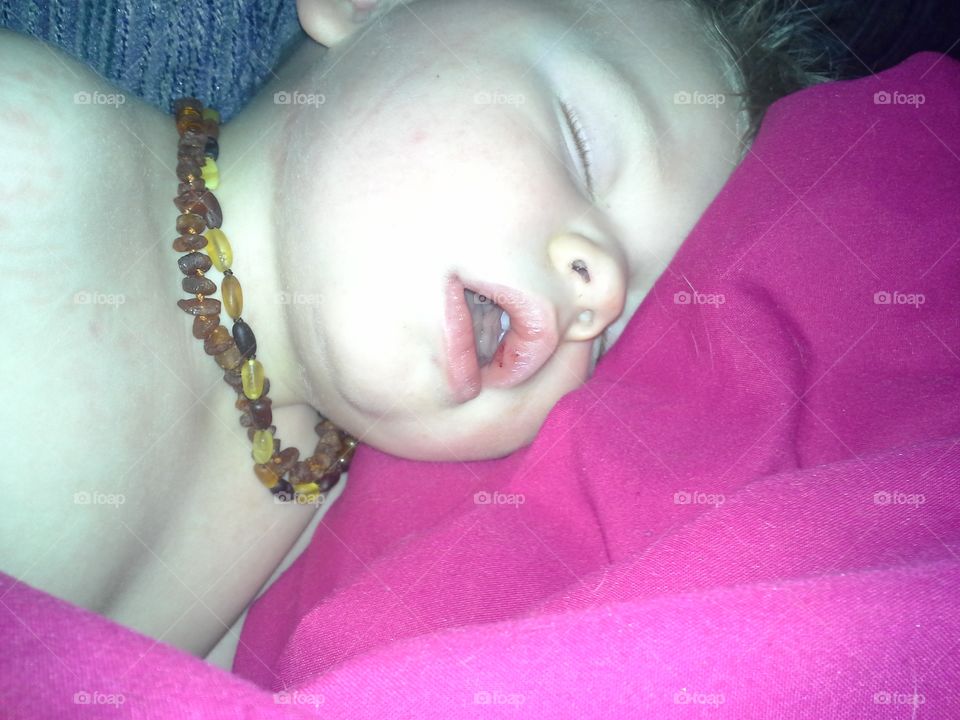 A blobde toddler boy sleeping with his mouth open on a pink blanket.