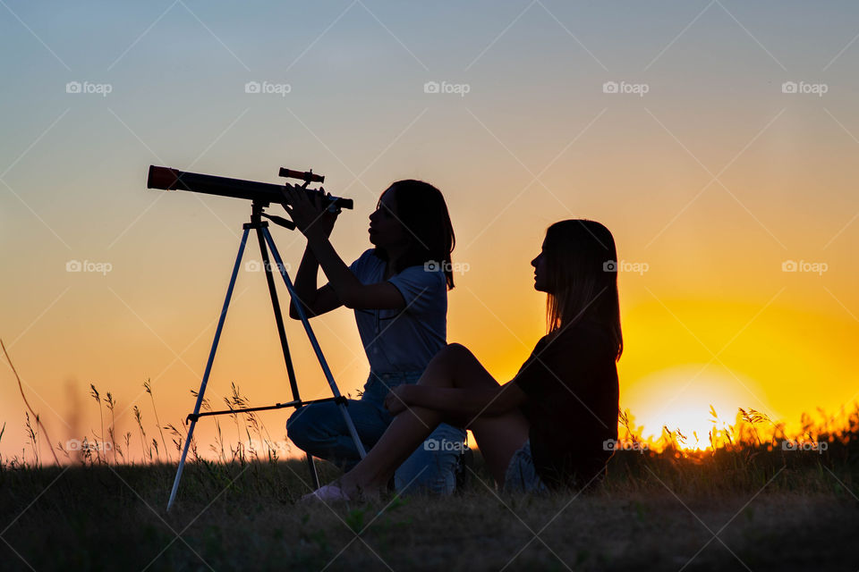 girls in the summer at sunset look through a telescope