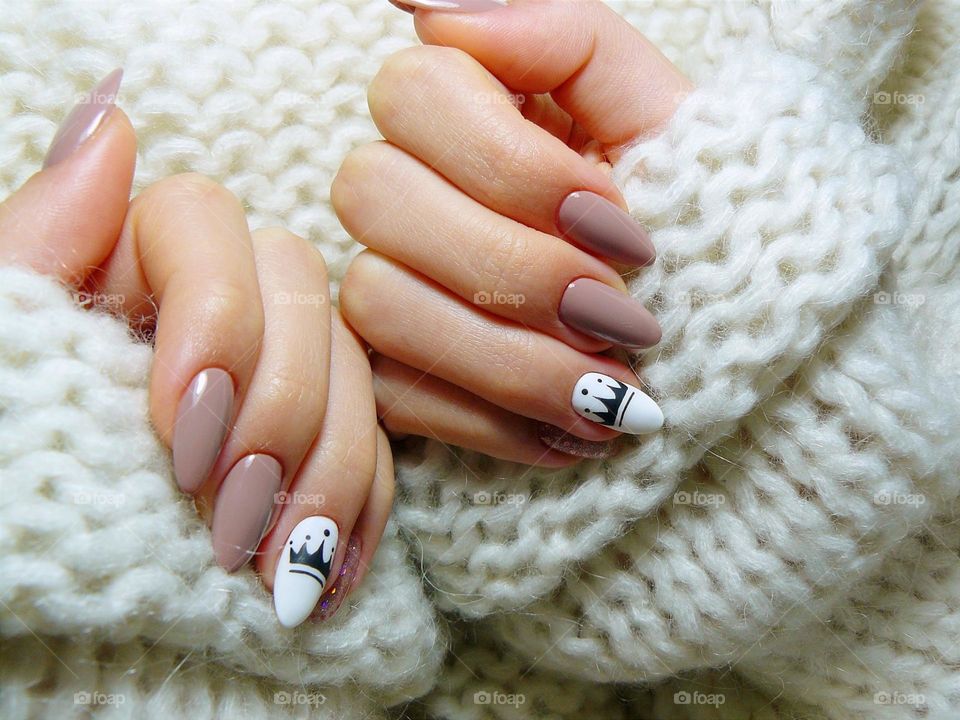 Gel nail manicure with pink polish and a crown design/ Beautiful polish on nails/ Naturally long nails with gel nail polish/Pink nails with a simple design up close in the light/Hands with a manicure in a sweater