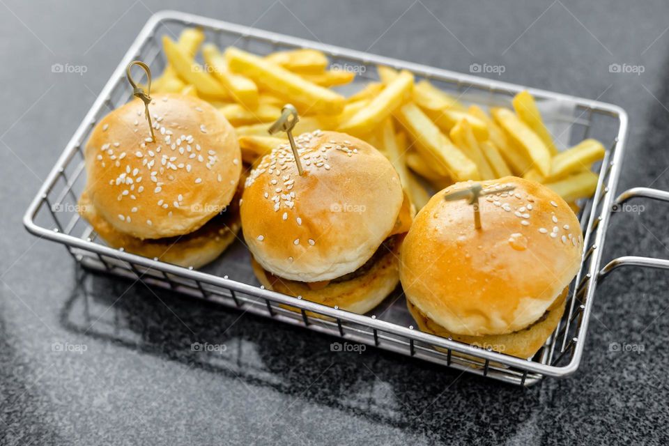 Delicious mini burgers and french fries on gray background 