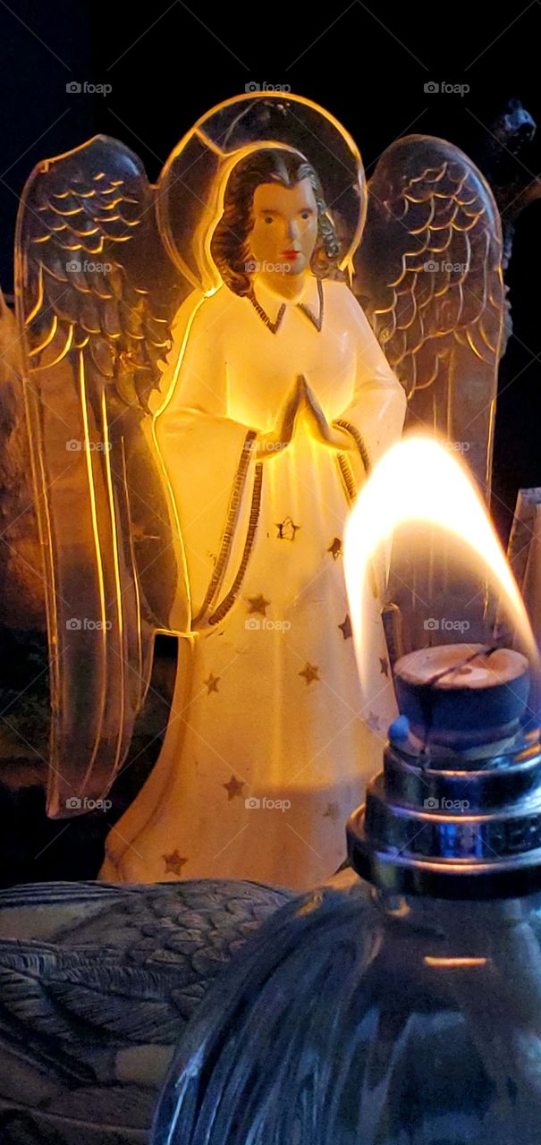 Vintage Angel nightlight next to Lampe Berger filled with scented oil. The wick on the burner has a flame burning before blown out. Various items lit by the low lighting.