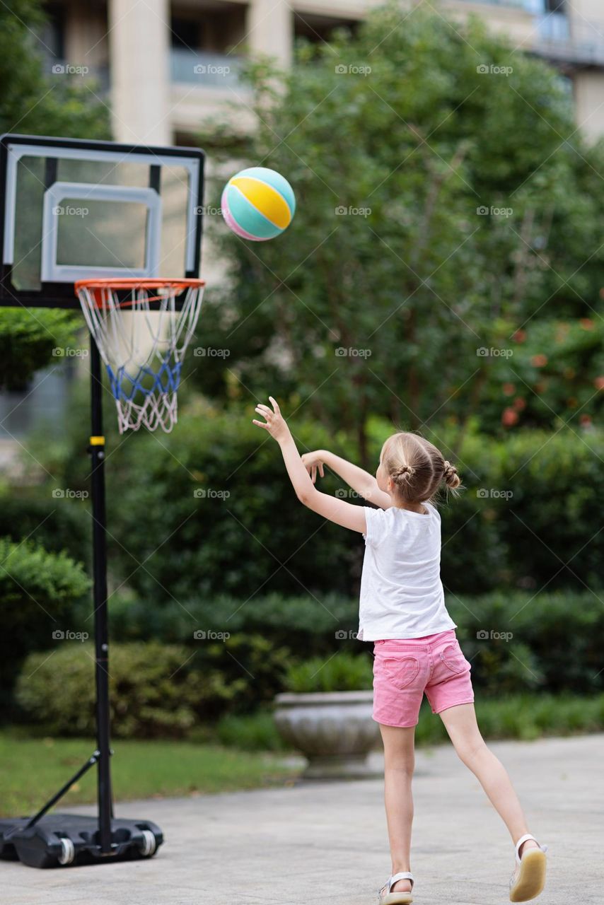 Little girl playing basketball on backyard 