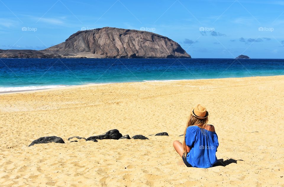 woman in summer hat sitting on thd samd on las conchas beach on graciosa canary island in Spain