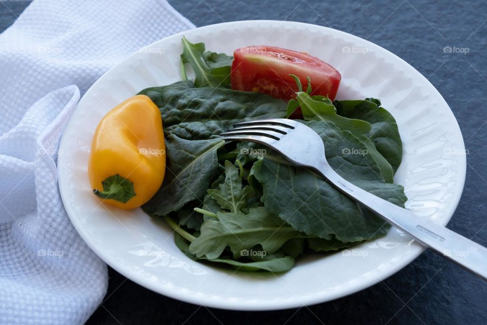 A close up of a white ceramic plate with lush and leafy spinach, red tomato and a orange pepper