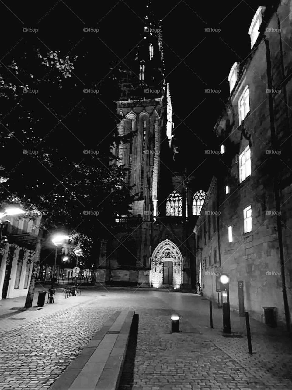 Black and white shot of a view of Quimper's cathedral and surrounding buildings with their illuminated stained glass windows and windows at night