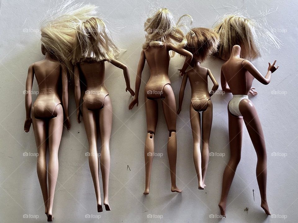 Five blonde Barbie dolls of various vintages face down without costumes on a white background 